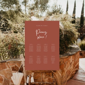 Peut inclure: Un plan de table brun avec du texte blanc. Le tableau est intitulé "Plan de Table" et dit "Prenez place !" en cursive. Le tableau liste les tables 1 à 8 avec les noms des invités à chaque table.