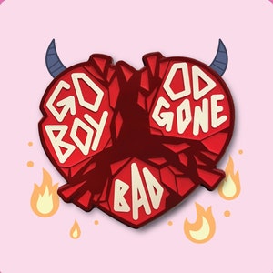 May include: A red heart-shaped pin with the words "GO BOY" and "GOD GONE BAD" in white block letters. The pin has blue devil horns and flames. The background is light pink.