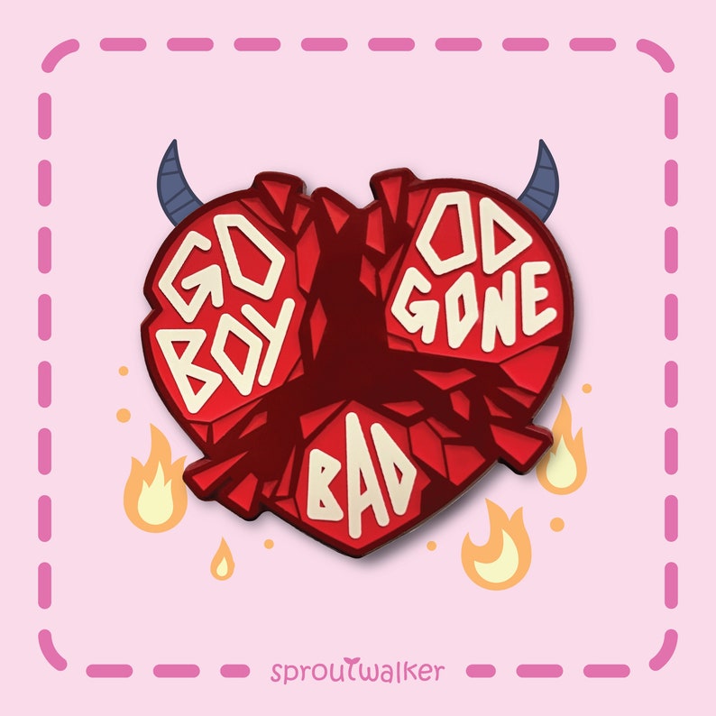 May include: A red heart-shaped pin with the words "GO BOY" and "GOD GONE BAD" in white block letters. The pin has blue devil horns and flames. The background is light pink.
