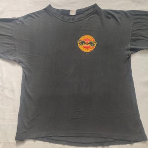 Könnte beinhalten: Schwarzes T-Shirt mit einem roten und gelben Logo, auf dem "Verbal Assault" mit zwei Augen in der Mitte steht.