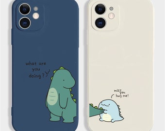 May include: Two phone cases featuring dinosaur designs. One is navy blue with a green dinosaur and the text "what are you doing?". The other is off-white with a blue dinosaur and the text "miss you hug me!"