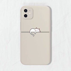 May include: A beige phone case featuring a white cat illustration sleeping on a line. The cat has pink cheeks and closed eyes.