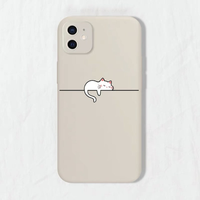 May include: A beige phone case featuring a white cat illustration sleeping on a line. The cat has pink cheeks and closed eyes.