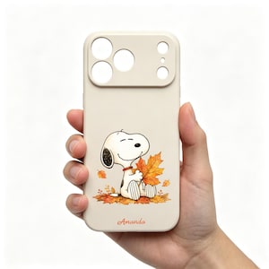 May include: A beige smartphone case featuring a cartoon dog sitting in a pile of orange and yellow autumn leaves. The dog has a red collar and is holding a large maple leaf. The name Amanda is printed in orange cursive script at the bottom.