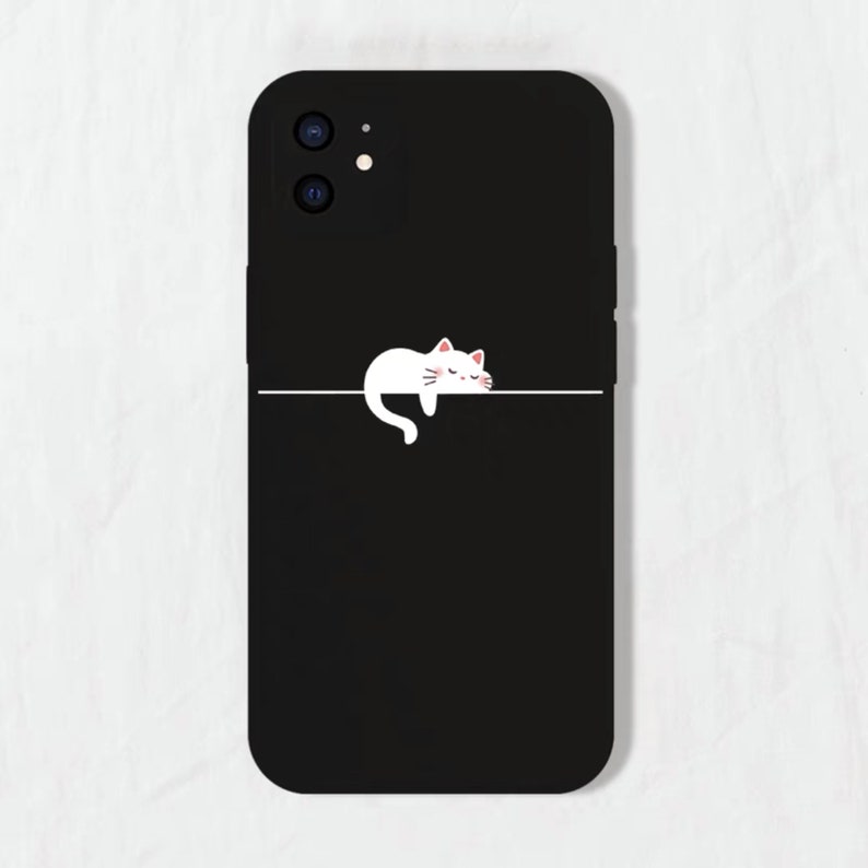 May include: Black phone case with a white cat illustration sleeping on a line. The phone case has a camera lens cutout.