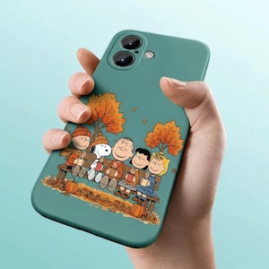 Può includere: Custodia per telefono turchese con un'illustrazione a cartoni animati di Snoopy e i suoi amici seduti su una panchina con foglie autunnali. Il design include zucche e personaggi che tengono tazze.