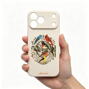 May include: A cream-colored phone case featuring a circular illustration of various colorful birds, including a blue jay, cardinal, and woodpecker, surrounded by green leaves and red berries. The name Amanda is printed in orange at the bottom.