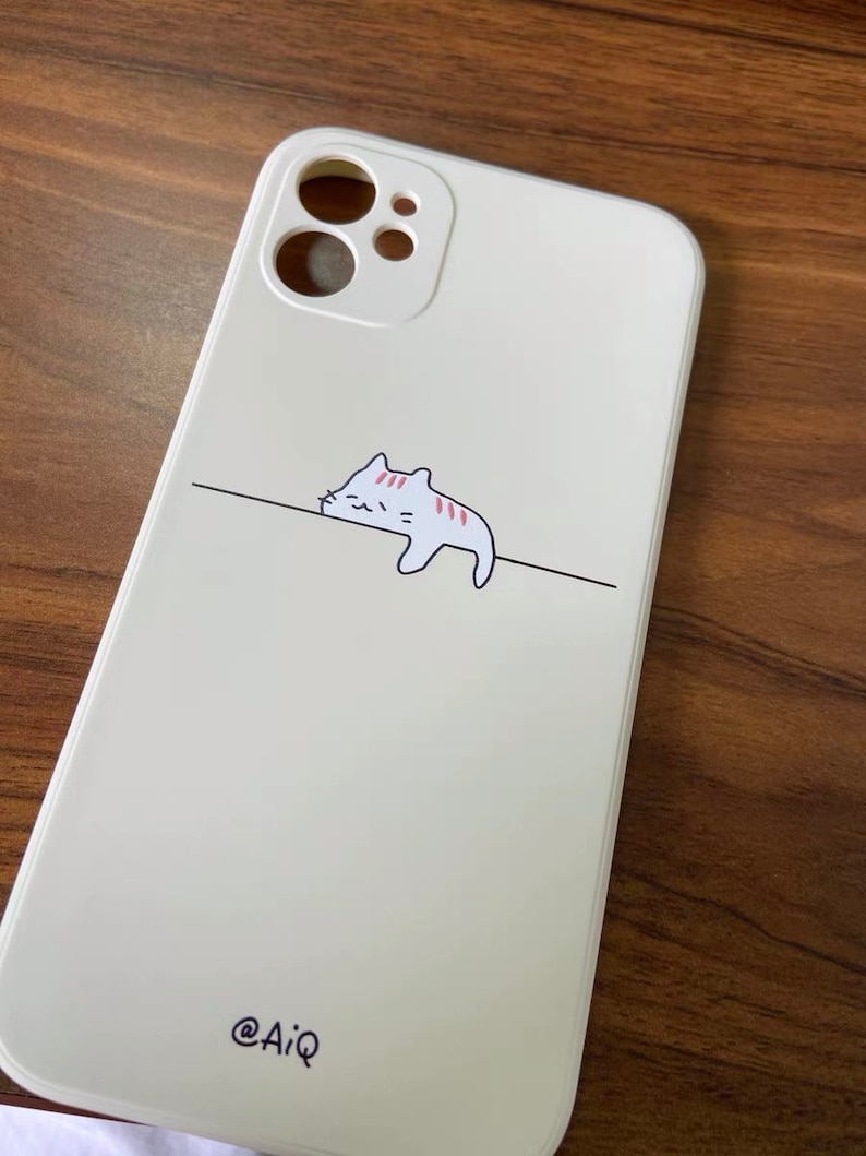 May include: White phone case with a cartoon cat design and the text "@AiQ" on the bottom.