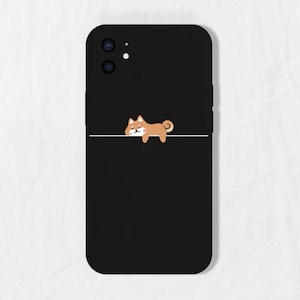 May include: Black phone case featuring a cute cartoon Shiba Inu dog illustration. The dog is brown and white and is lying down with its head resting on a white line.