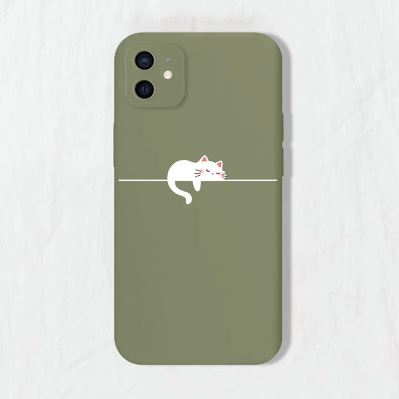 May include: A green phone case featuring a white cat illustration sleeping on a line. The case has a camera cutout with two lenses.