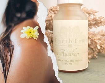Puede incluir: Una pequeña botella de vidrio ámbar con una etiqueta blanca que dice "Earth Temple" y "Awaken Essential Oil Blend 15 ml". La etiqueta tiene un diseño floral.