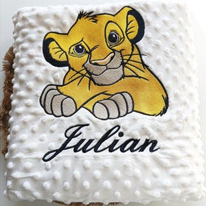 May include: White plush blanket with a yellow embroidered lion cub and the name "Julian" in black cursive.