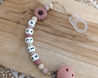 Può includere: Un portaciuccio con una serie di perline rotonde in silicone nei toni del rosa antico, beige e crema. Le perline compongono il nome AYLIE con lettere nere. Sono inclusi una perlina a forma di fiore rosa antico e un attacco rotondo.