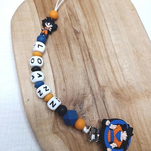 Può includere: Un fermaglio per ciuccio per bambini con un design di personaggi dei cartoni animati. La clip presenta una serie di perline di vari colori, tra cui bianco, arancione, nero e blu. La clip ha una chiusura in metallo e un cordino per attaccare un ciuccio.