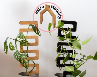 May include: Two plant stands, one black and one natural wood, with a potted plant on each. The stands are designed to help plants grow upwards and have a unique shape. The text "extra stability" is written in a circle around the top of the natural wood stand.