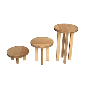 Peut inclure: Trois présentoirs ronds en bois à étages avec une finition en bois naturel. Les présentoirs sont de tailles différentes et sont disposés par ordre de taille, du plus petit au plus grand.