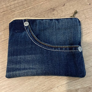 以下が含まれることがあります： 前面にポケットと2つの銀色のリベットが付いた、小さな青いデニムのジッパー付きポーチ。ポーチはリサイクルデニムで作られています。