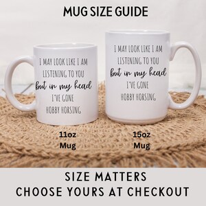 May include: Two white ceramic mugs with black text. The text on both mugs reads "I may look like I am listening to you but in my head I've gone hobby horsing". The mug on the left is labeled "11oz Mug" and the mug on the right is labeled "15oz Mug".