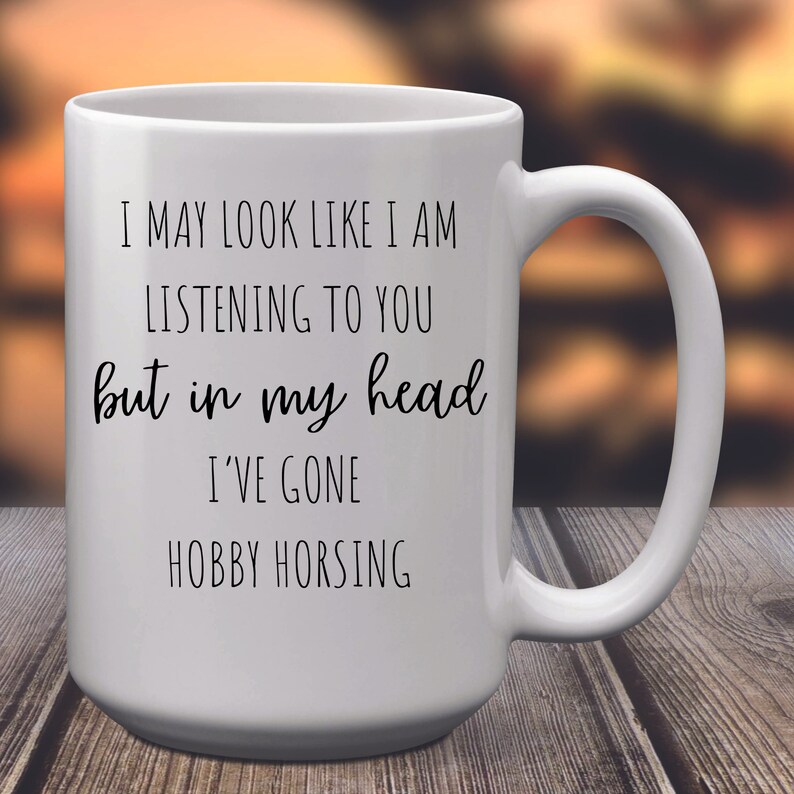 May include: White ceramic coffee mug with black text that reads "I may look like I am listening to you but in my head I've gone hobby horsing."
