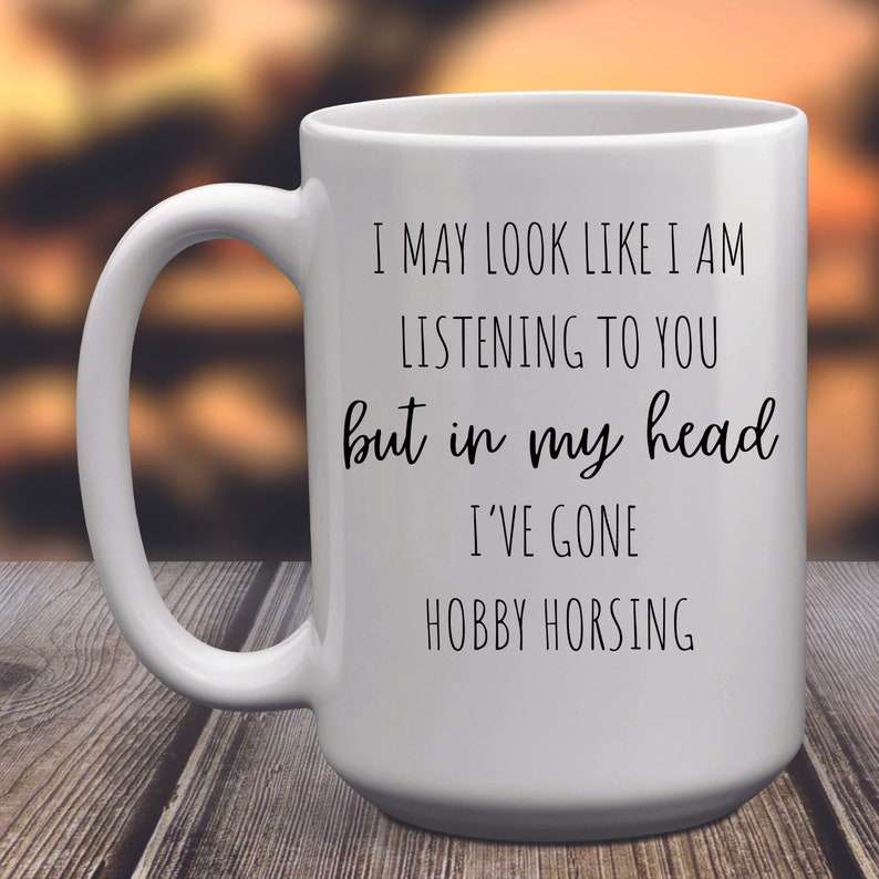 May include: White ceramic coffee mug with black text that reads "I may look like I am listening to you but in my head I've gone hobby horsing."
