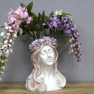 May include: White ceramic planter shaped like a woman's bust with a crown of pink flowers. The planter is decorated with pink and purple flowers.