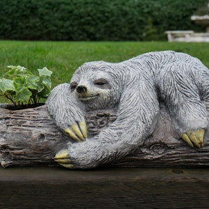 May include: A grey sloth sculpture in a relaxed pose, resting on a log planter with green ivy growing inside. The planter is made of concrete and has a realistic wood texture.