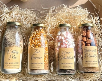 Pode incluir: Quatro garrafas de vidro cheias de ingredientes para fazer guloseimas. As garrafas são etiquetadas com "Keksteig Mix", "Zint Popcorn", "Warme Schokolade" e "Gebrannte Mandeln". Cada garrafa tem instruções para fazer a guloseima, "Zum Selber Machen".