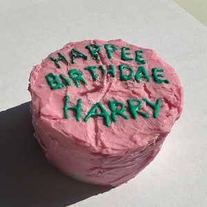Könnte beinhalten: Ein rosa glasierter Kuchen mit grünem Zuckerguss, auf dem "Happy Birthday Harry" steht.