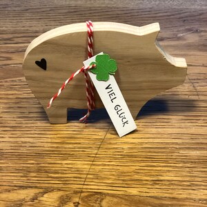 May include: Wooden piggy bank with a red and white string tied around it. A green shamrock and a tag that says "VIEL GL&Uuml;CK" are attached to the string.