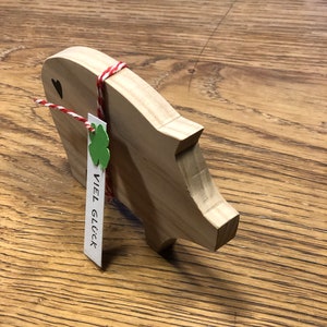 May include: Wooden piggy bank with a red and white string tied around it. A small green shamrock and a tag with the text "VIEL GL&Uuml;CK" are attached to the string.