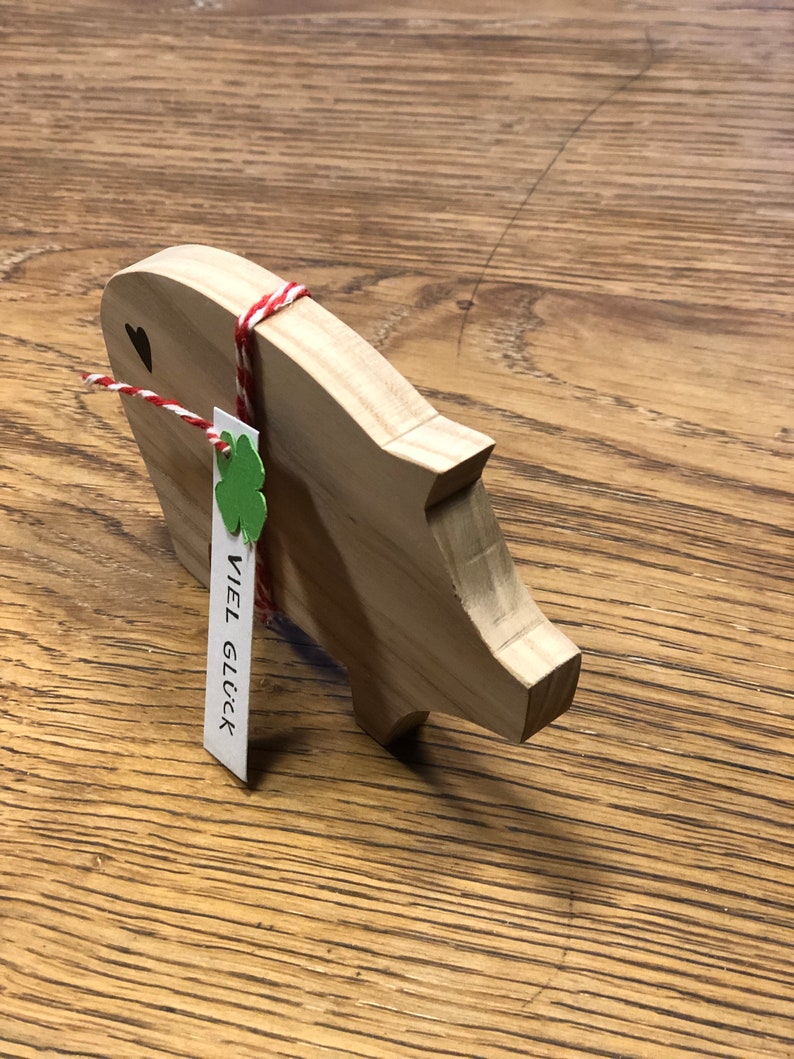 May include: Wooden piggy bank with a red and white string tied around it. A small green shamrock and a tag with the text "VIEL GL&Uuml;CK" are attached to the string.