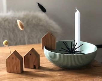May include: Three small wooden houses with a single window each, a white candle, and a black metal starburst on a green bowl, all on a wooden table.