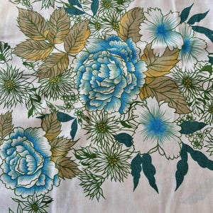 Puede incluir: Tela blanca con un patrón floral azul y verde. El patrón presenta grandes flores azules con centros blancos y hojas verdes.