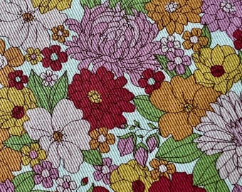 May include: A close-up of a floral pattern featuring a variety of flowers in shades of yellow, orange, red, and purple. The flowers are set against a light blue background with green leaves.