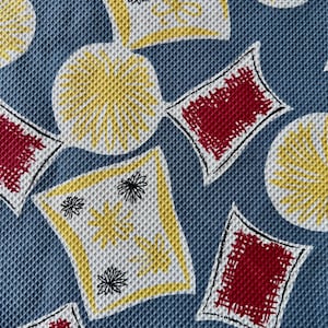 May include: A textured fabric featuring a repeating pattern of blue, yellow, and red shapes. The design includes yellow circles with radiating lines, white diamond-like shapes with yellow borders and black floral accents, and solid red squares.