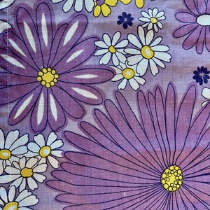 Puede incluir: Primer plano de una tela con un estampado floral. Grandes margaritas moradas con centros amarillos y flores de pétalos blancos están dispersas sobre un fondo morado claro. Pequeñas flores azules llenan los espacios entre las flores más grandes.