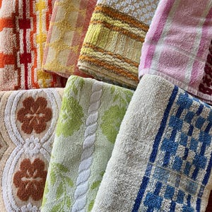 May include: A collection of seven folded terry cloth towels featuring various patterns and colors, including orange, yellow, pink, green, brown, and blue. The textures include floral motifs, geometric grids, and striped designs in cotton fabric.