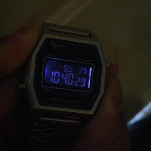 May include: A silver digital wristwatch with a black face. The watch face displays the time 10:40:29, the day of the week 'SU', and the date '29'. The watch face also has the words 'Armitron', 'Start Stop', 'Mode', 'Light', and 'Water Resist'.