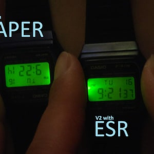 May include: Two black digital watches with illuminated green displays. The left watch shows "22:6" and the right watch shows "9:2 137". Text on the image reads "V2 with PAPER" and "V2 with ESR".