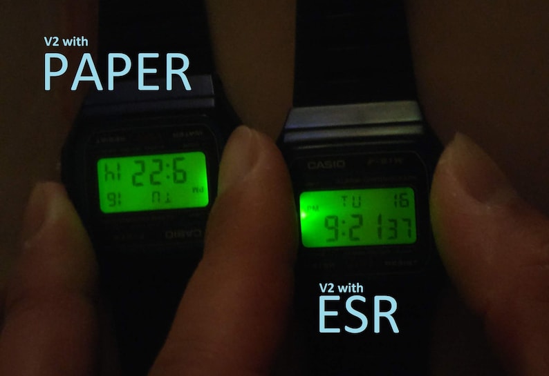 May include: Two black digital watches with illuminated green displays. The left watch shows "22:6" and the right watch shows "9:2 137". Text on the image reads "V2 with PAPER" and "V2 with ESR".