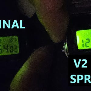 May include: Two digital watches with illuminated green displays showing the time. The left watch displays "1:54:03" and the right watch displays "12:57:25". Text in the image reads "ORIGINAL" and "V2 LIGHT SPREADER".
