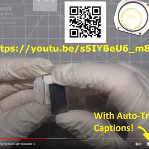 May include: A person wearing white gloves is holding a small, white electronic component with a black screen. Other disassembled electronic parts and a QR code are visible. Text on the screen reads "With Auto-Translated Captions!" and a YouTube URL is visible.