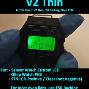 May include: Black Casio F-91W digital watch with a green illuminated display showing the time. The watch face displays the text "CASIO" and "F-91W". The image also includes the text "V2 Thin" and other technical details about the watch.