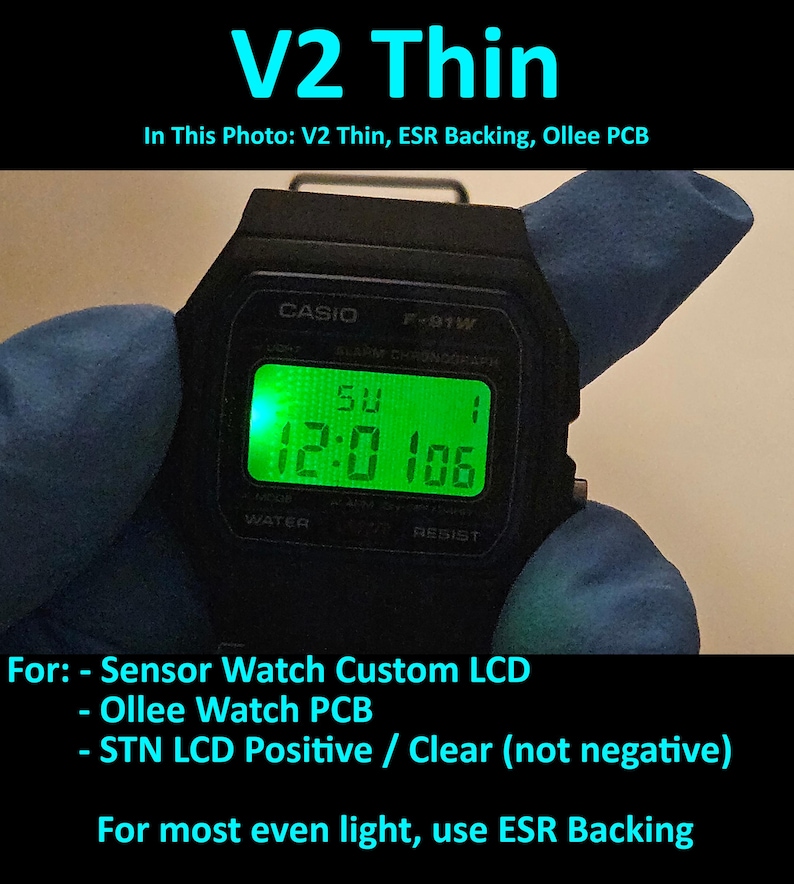 May include: Black Casio F-91W digital watch with a green illuminated display showing the time. The watch face displays the text "CASIO" and "F-91W". The image also includes the text "V2 Thin" and other technical details about the watch.