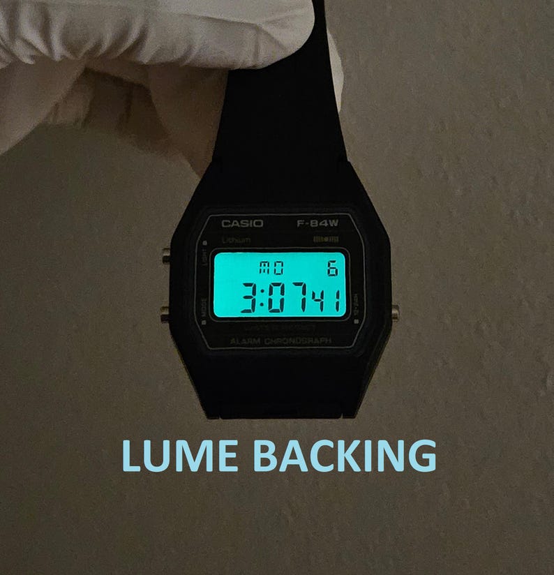 May include: A black Casio F-94W digital watch with a glowing green display showing the time. The watch face displays the day and date. The text "LUME BACKING" is below the watch.