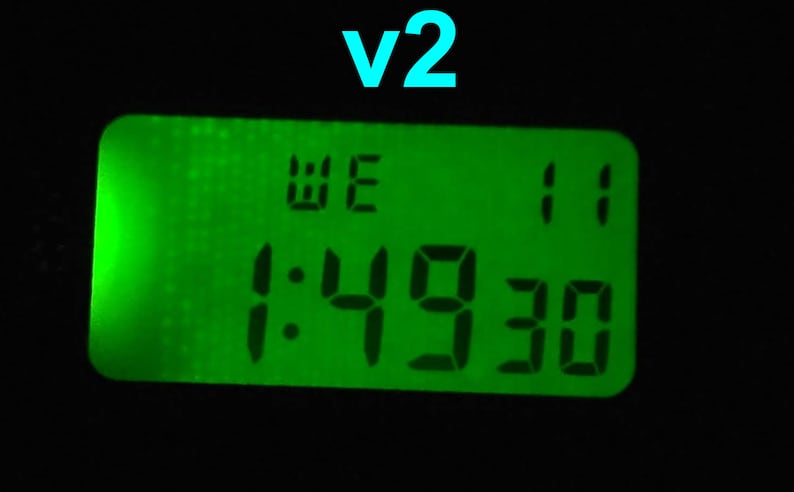 May include: A digital clock with a green display showing the time as 1:49:30. The word "WE" is displayed above the time, and the number "11" is displayed to the right. The text "v2" is displayed above the clock.