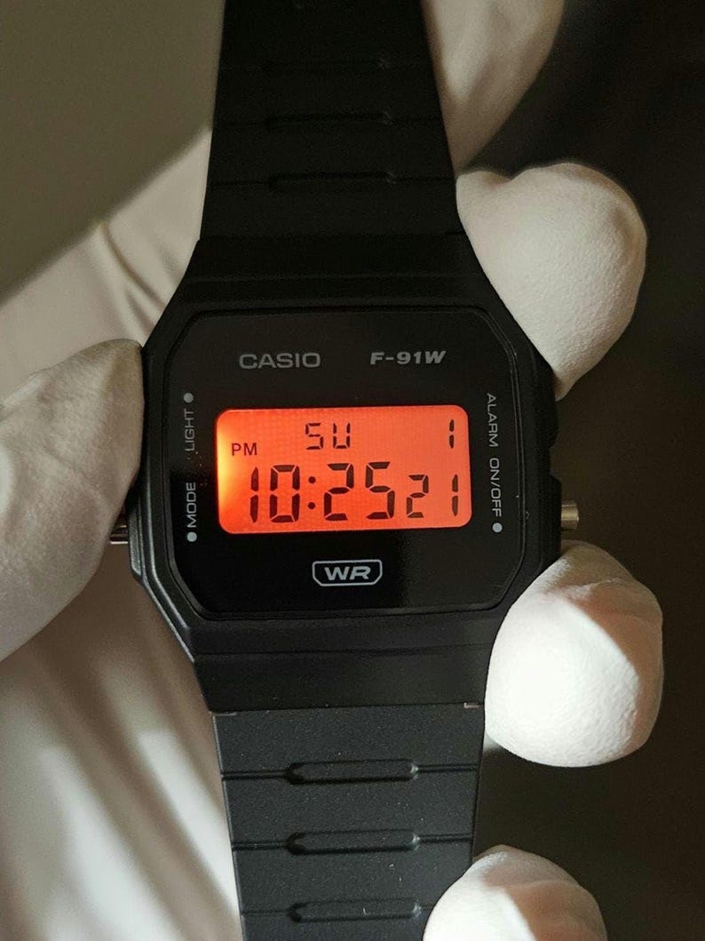 May include: A black Casio F-91W digital watch with a red digital display showing the time 10:25:21 PM. The watch is water resistant and has an alarm function.