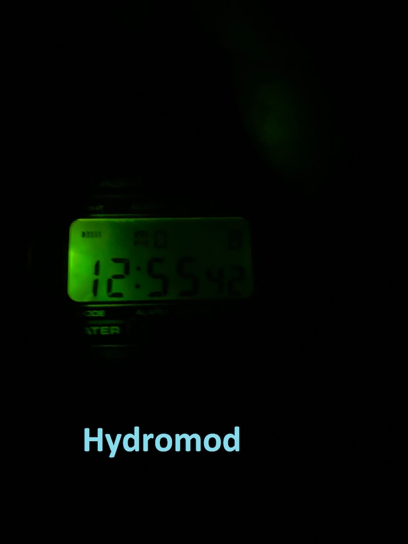 May include: A digital clock with a green illuminated display showing the time as 12:55:42. The word "Hydromod" is displayed in light blue text below the clock against a black background.