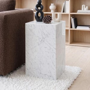 Pode incluir: Uma mesa lateral de mármore branco com veios cinzentos. A mesa quadrada está ao lado de um sofá castanho estofado e de um tapete branco. Os itens decorativos na mesa incluem uma escultura preta, uma vagem de semente seca e um vaso branco.