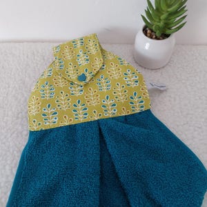 Peut inclure: Un essuie-main suspendu composé d'une partie inférieure en tissu éponge bleu sarcelle et d'une partie supérieure en tissu vert olive ornée d'un motif répétitif de feuilles blanches et sarcelle. Le rabat se ferme par un bouton-pression bleu sarcelle.